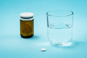 Supplement or medicine bottle and pill with water glass on blue background