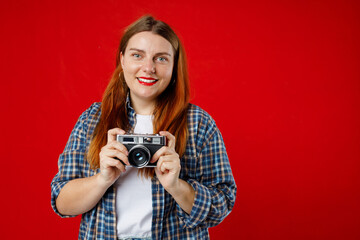 Portrait of a smiling young woman standing with photo camera isolated over red background. Home hobby, lifestyle, travel, people concept