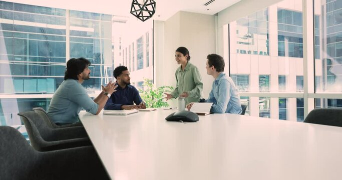 Four multiethnic colleagues discussing new joint project met in conference room in modern skyscraper office. Teamwork, partnership, corporate briefing event of professional team members. Business talk
