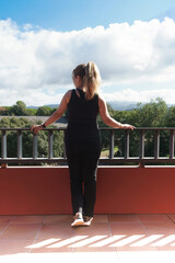 Rear view of a young girl with pony tail leaning out of a balcony looking at the landscape.Rear...