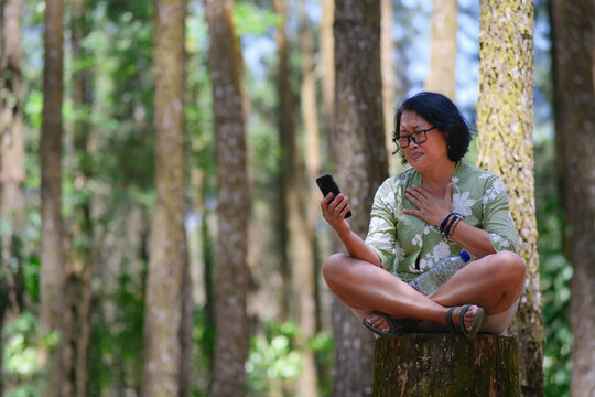 Very sad facial expression of a woman sitting alone in the park after reading messages on her smartphone