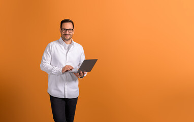 Portrait of successful businessman doing research over laptop while standing on orange background
