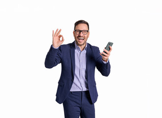 Portrait of cheerful businessman with mobile phone screaming and showing OK sign on white background