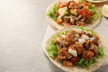 Delicious tacos with vegetables and meat on light table, space for text
