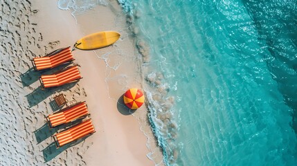 Top view of Beach chairs, surfboard, and beach ball on a sandy shore with clear blue water with copy space on left side