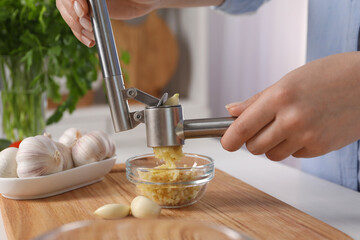Woman squeezing garlic with press at white table indoors, closeup - obrazy, fototapety, plakaty