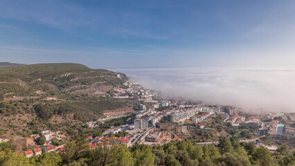 Obraz premium Panorama showing aerial View of Sesimbra Town and Port covered by fog timelapse, Portugal.