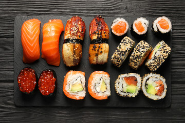 Set of delicious sushi rolls on black wooden table, top view