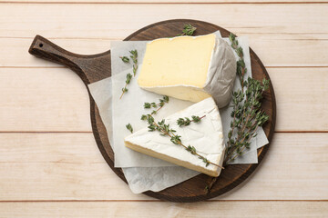 Board with pieces of tasty camembert cheese and thyme on light wooden table, top view