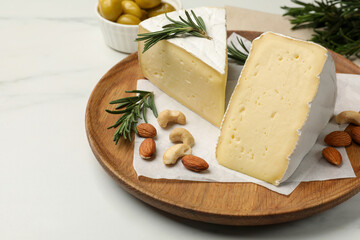 Plate with pieces of tasty camembert cheese, nuts and rosemary on white table, closeup. Space for...