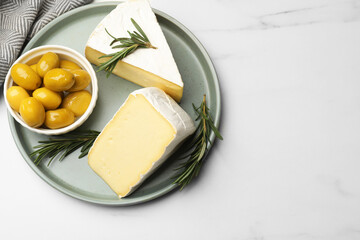 Plate with pieces of tasty camembert cheese, olives and rosemary on white table, top view. Space for text