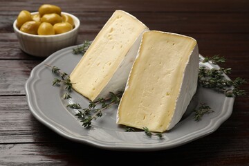 Pieces of tasty camembert cheese and thyme on wooden table, closeup