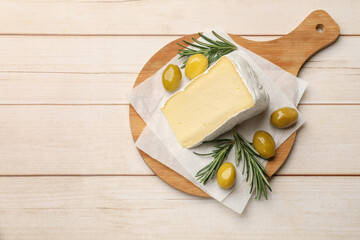 Board with piece of tasty camembert cheese, olives and rosemary on light wooden table, top view....