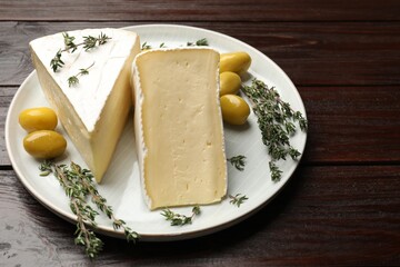 Plate with pieces of tasty camembert cheese, olives and rosemary on wooden table, closeup