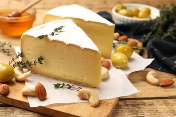 Tasty Camembert cheese with thyme, olives and nuts on wooden table, closeup