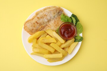 Delicious fish and chips with ketchup, spinach and lettuce on yellow table, top view
