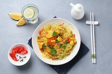 Stir-fry. Delicious cooked noodles with chicken and vegetables in bowl served on gray textured table, flat lay