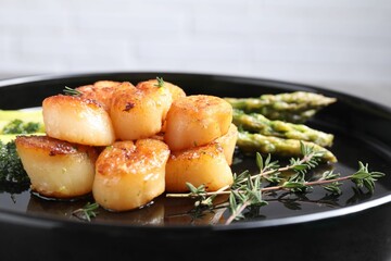 Delicious fried scallops with asparagus and thyme on plate, closeup