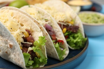 Delicious tacos with meat and vegetables on light blue table, closeup