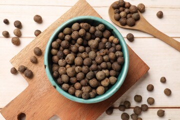 Dry allspice berries (Jamaica pepper) in bowl and spoon on light wooden table, flat lay