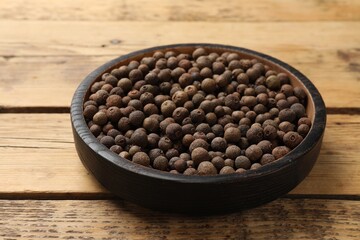 Aromatic allspice pepper grains in bowl on wooden table, closeup
