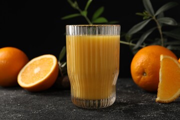 Tasty fresh oranges, juice and leaves on black table, closeup