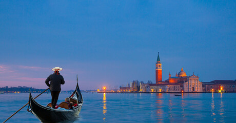 Venetian gondolier punting gondola through grand canal waters - View of San Giorgio Island in...
