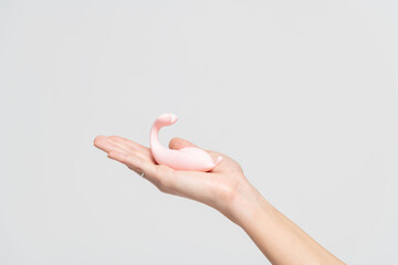 Close-up view of adult caucasian woman holding in her hand small pink vibrator against gray background. Soft focus. Adult sex toys theme. - obrazy, fototapety, plakaty