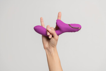 Close-up view of adult caucasian woman holding in her hand purple vibrator against gray background....