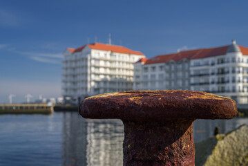 A CITY BY THE SEA - Old rusty bollard on the port quay and a holiday resort in the background
