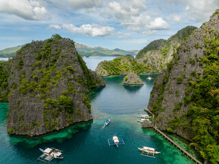 Boats over green water surrounded by splendid limestone rocks in islands. Kayangan Lake. Coron,...