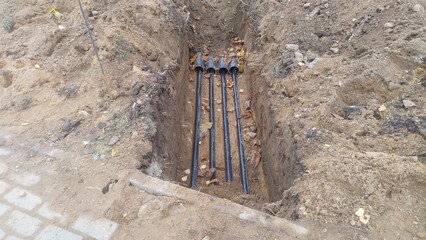A trench was dug next to the concrete tile walkway to replace cables, pipes and other utilities. The soil removed from the trench is lying on the sides of the trench with a rebar sticking out of it