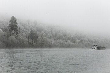 péniche avançant sur un cours d'eau au bord d'une forêt gelée, le tout dans le brouillard de...