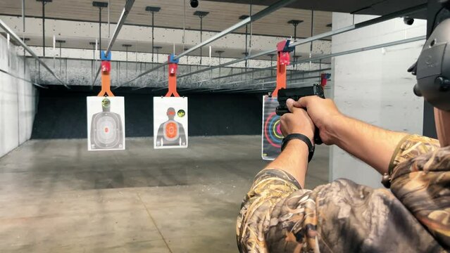 Man Practicing at Indoor Shooting Range, A man in camo attire aiming a handgun at targets in an indoor shooting range.