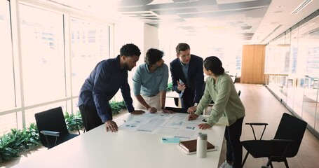 Diverse businesspeople discuss financial report in charts and diagrams, analysing infographics, review sales statistics, prepare presentation, engaged in brainstorm, analyzing profit at group meeting