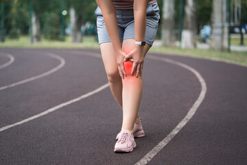 Diseases of the knee joint, bone fracture and inflammation, athletic woman on a running track after workout suffering from pain in leg and doing self-massage - 749945047