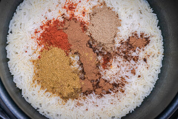 A casserole or large saucepan filled with white basmati rice with various spices on top: cumin, red...