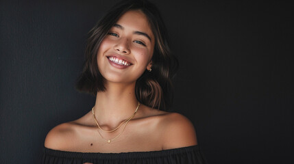 Against a matte black background, a chic young woman with a sleek lob haircut, wearing an off-the-shoulder shirt and delicate gold jewelry, beams with confidence