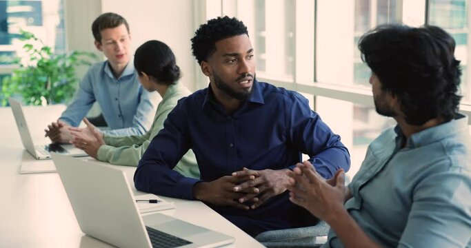 African and Indian workmates lead discussion met in co-working office, sit at desk with laptop, share ideas, think on issue solution, pondering on marketing strategy. Teamwork, business, cooperation