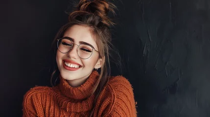 Foto op Canvas Smiling merrily against a warm dark backdrop is a stylish young lady with a messy bun, wearing trendy glasses and a snug oversized sweater © Stone Shoaib