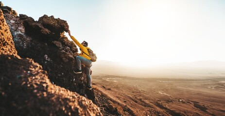 Male hiker climbing the mountain - Strong hiker standing on the top of the cliff enjoying sunset view - Extreme sport life style concept - 749953266