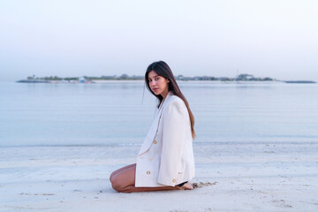 Fototapeta na wymiar Beautiful Middle Eastern woman sitting on the beach wearing jacket
