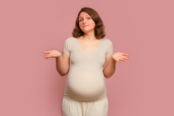 A doubting pregnant woman on a studio pink background. Pregnancy in a thoughtful woman with a...