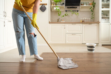 A woman mops the floor in her home kitchen. Female hands in yellow gloves while cleaning the kitchen