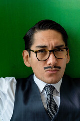 Eccentric Latin man wearing glasses making facial expression looking at camera on the green background