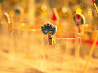 Close up of a colorful Purim mask clip on a glittery cup with blurred festive background