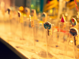 Colorful traditional cocktail stirrers in glasses, with blurred background, warm lighting, festive ambiance.