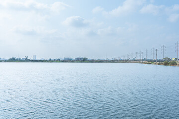 Cityscape by the River A serene view blending urban and natural elements, featuring water, sky, clouds, and a distant city with a bridge, boats, and reflections under the warm hues of a summer sunset