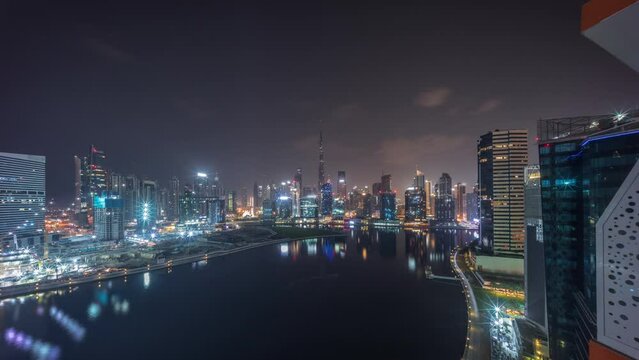 Aerial panoramic view to Dubai Business Bay and Downtown with the various skyscrapers and towers along waterfront on canal night timelapse during all night. Construction site with cranes
