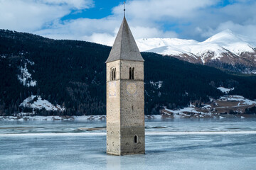 Curon, submerged bell tower of Resia. In winter with the frozen lake.